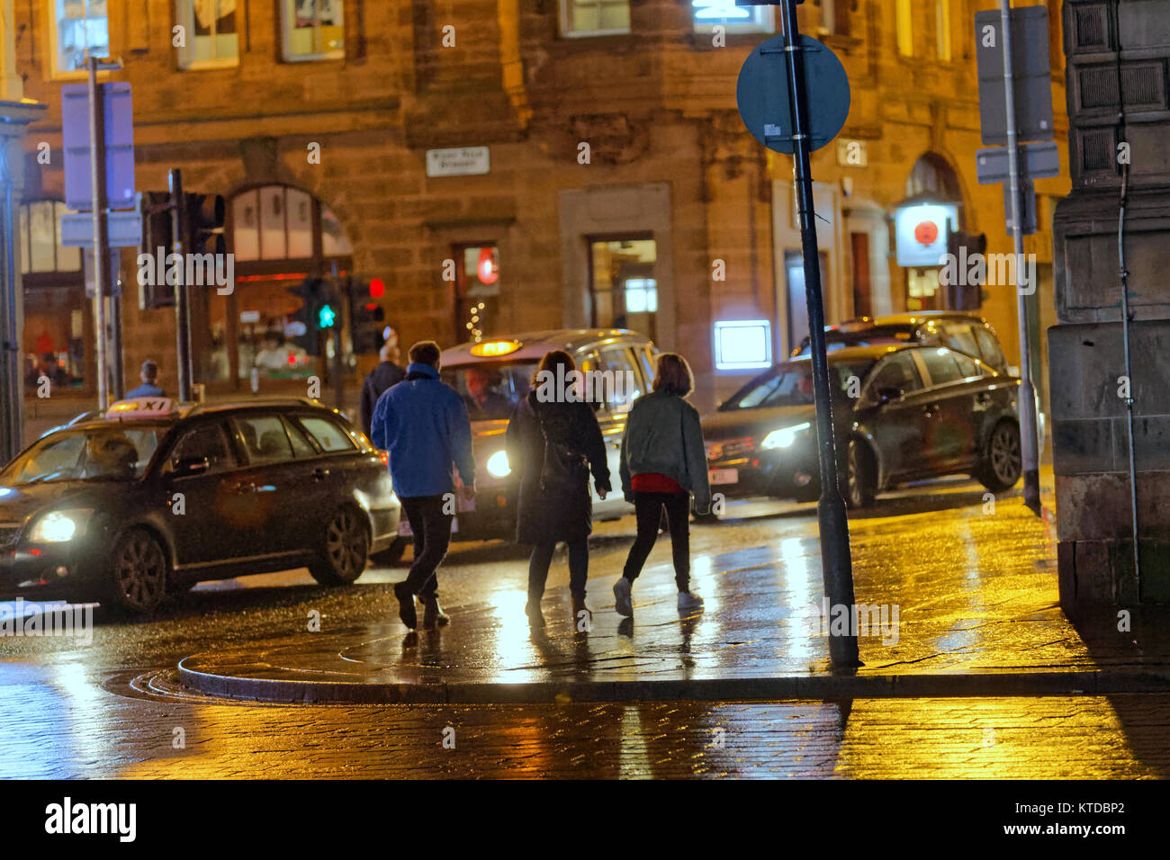 Il grintoso urban notte tempo umido di Glasgow la vita di strada tre giovani uomini a camminare sulla strada tra barre insieme a tarda notte Foto Stock