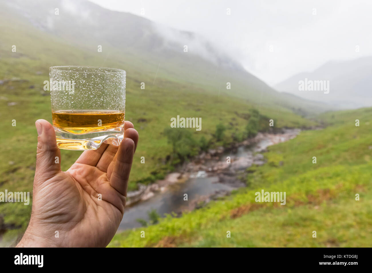 Gran Bretagna, Scozia, Highlands scozzesi, Glen Etive con fiume Etive e Glen Etive Falls, mano azienda scotish whiskey in un bicchiere Foto Stock