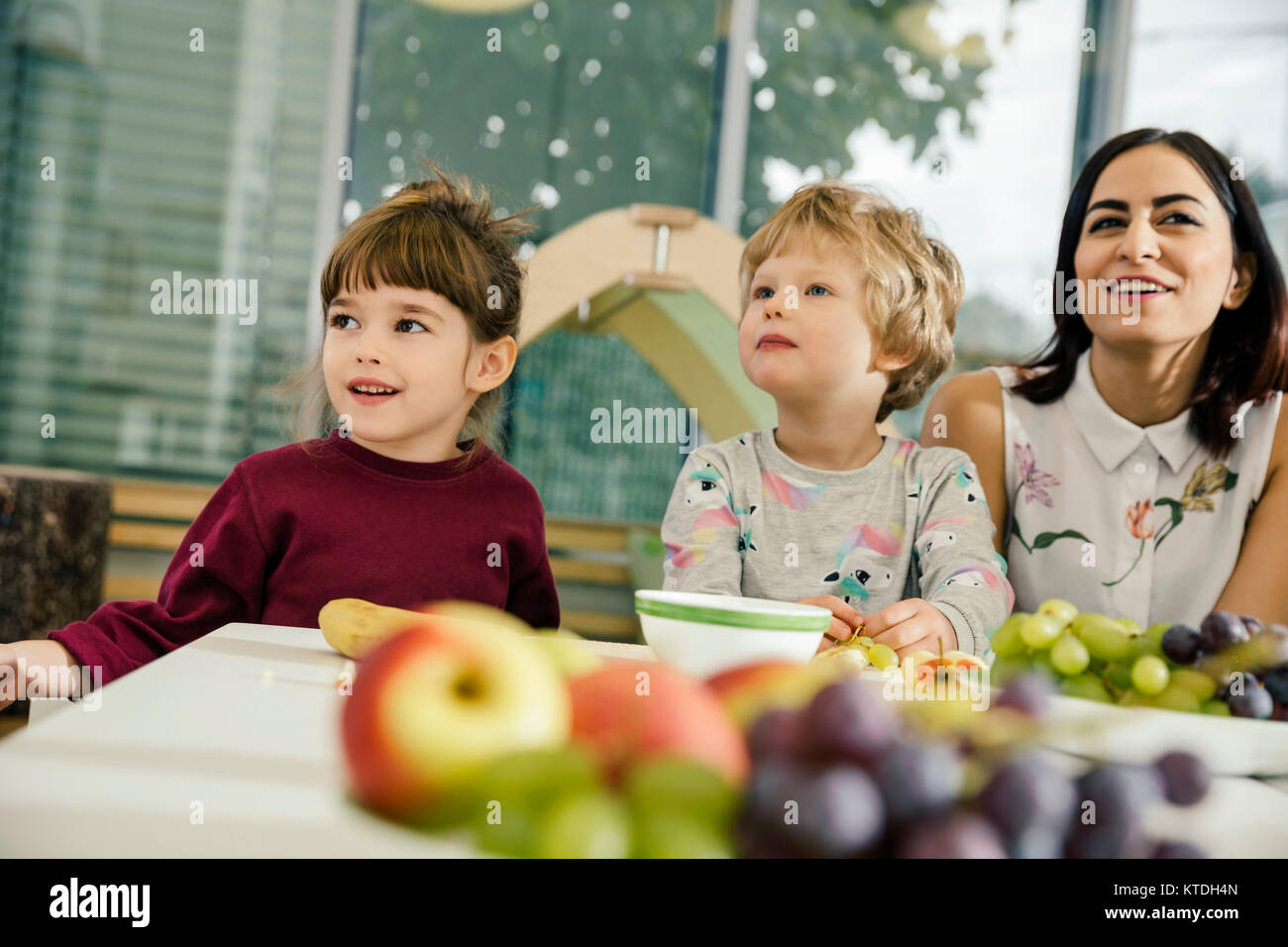 I bambini e il maestro seduta a tavola con la frutta nella scuola materna Foto Stock