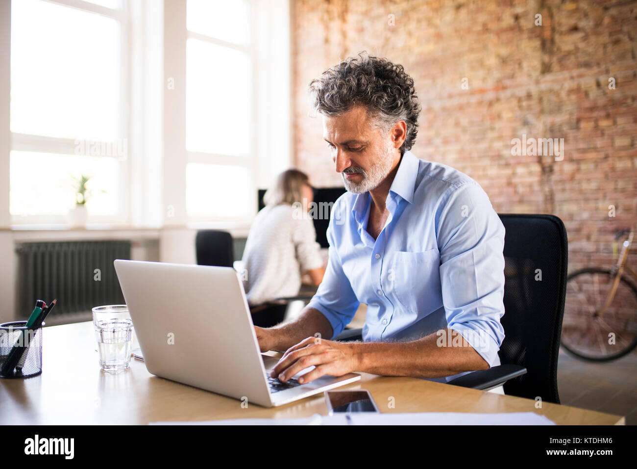 Uomo d affari con computer portatile in ufficio con il collega in background Foto Stock