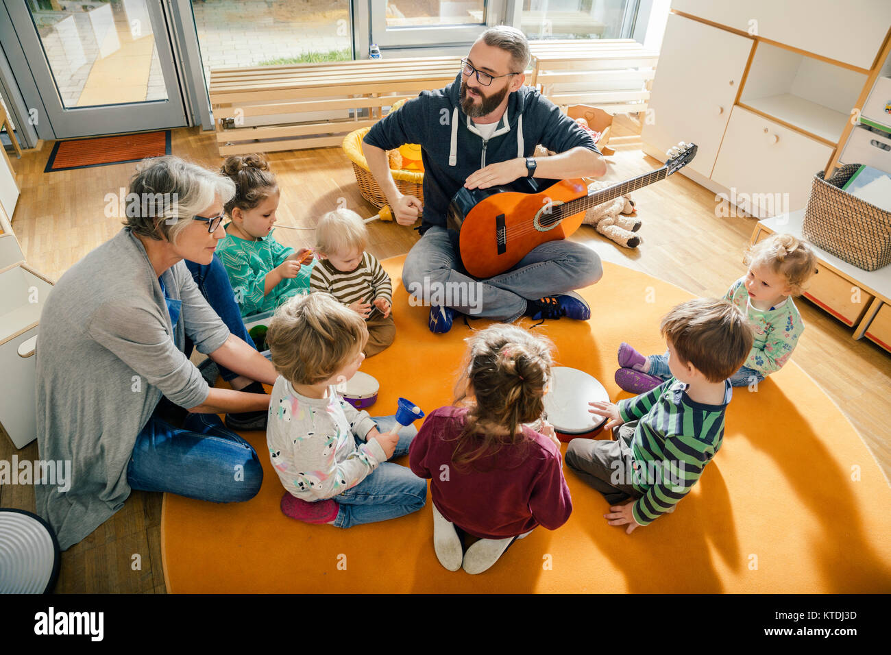 I bambini e gli insegnanti di canto e di fare musica in una scuola materna Foto Stock