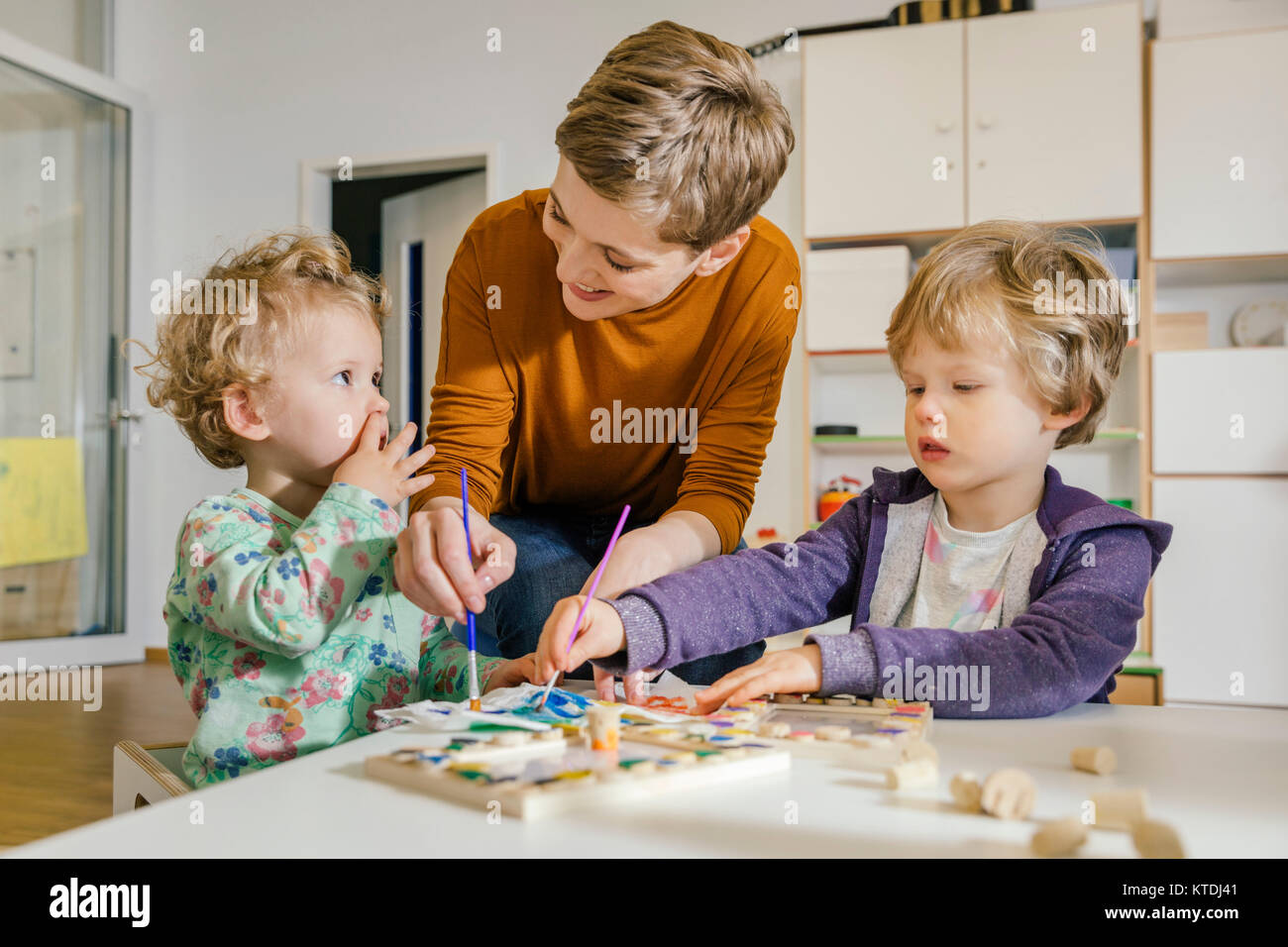 Pre-insegnante di pittura con due bambini in una scuola materna Foto Stock