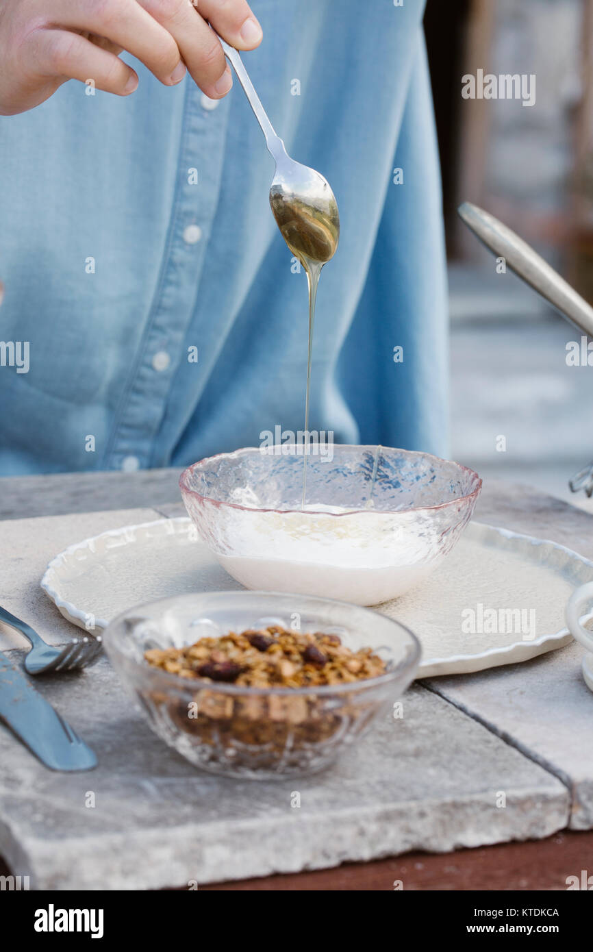 L'Italia, donna gocciolamento del miele per lo yogurt naturale al tavolo per la colazione sulla terrazza, vista parziale Foto Stock