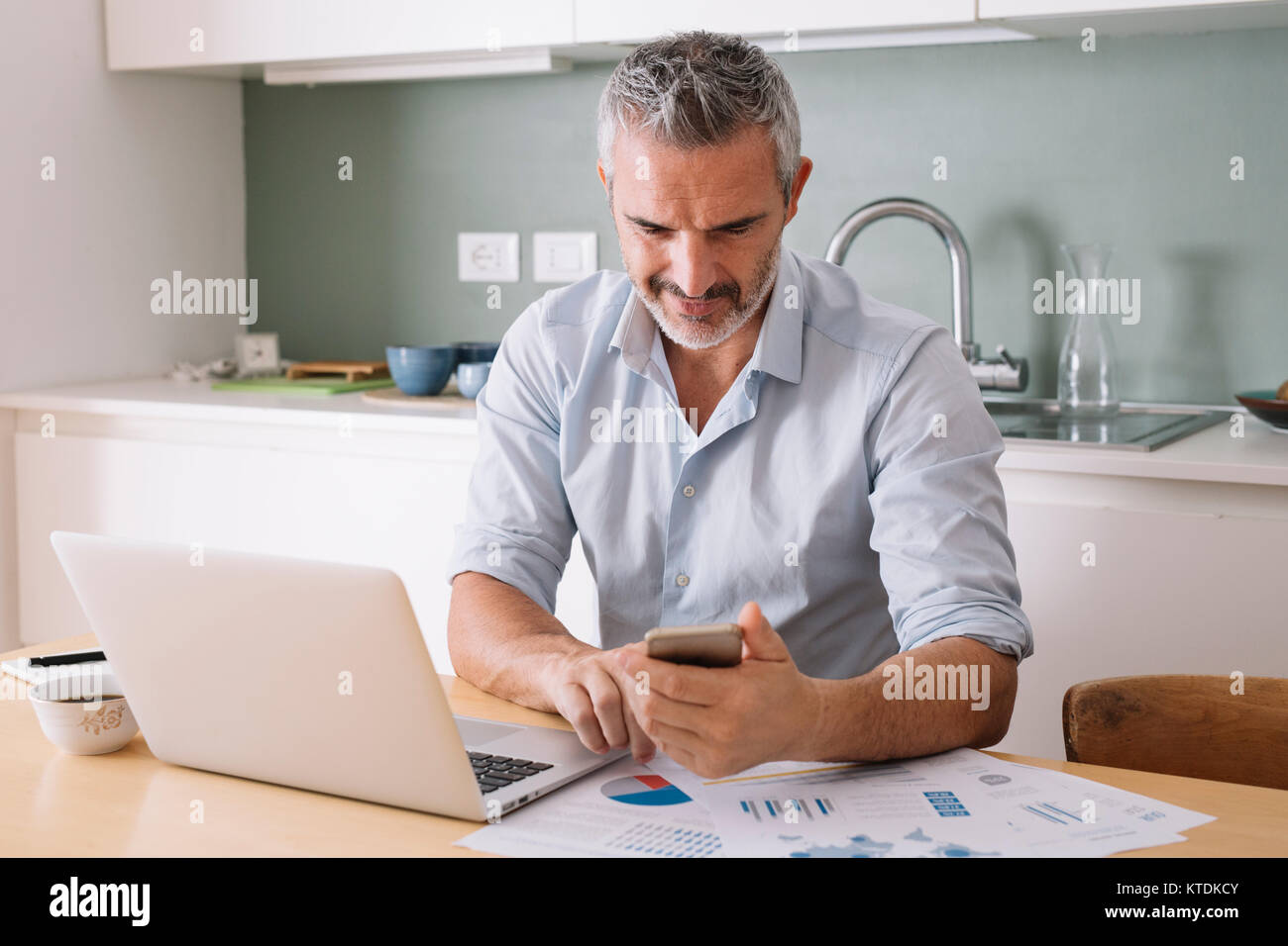 Uomo di analisi dei dati e utilizzo di computer portatile e un telefono cellulare in home office Foto Stock
