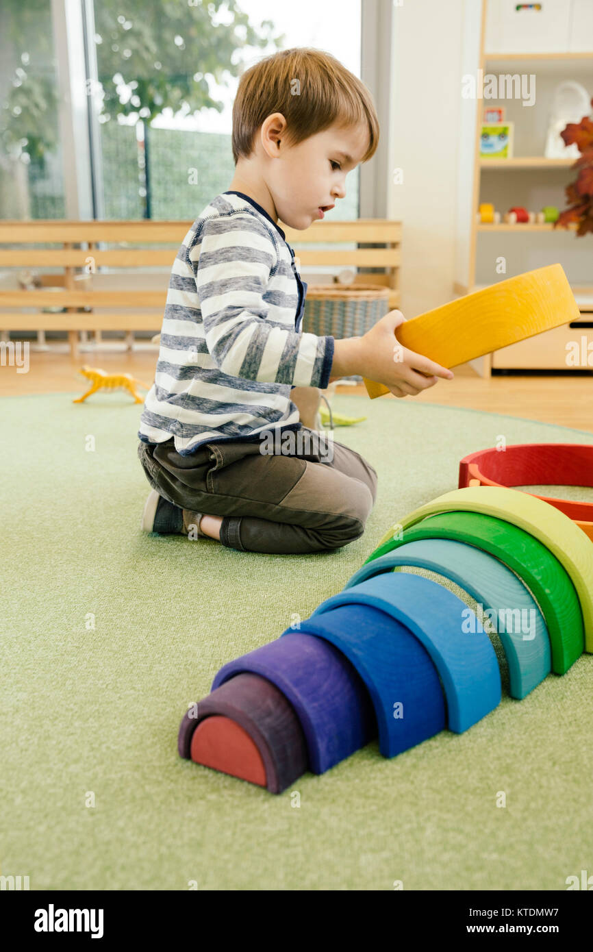 Ragazzo giocando con legno forme arcobaleno nella scuola materna Foto Stock