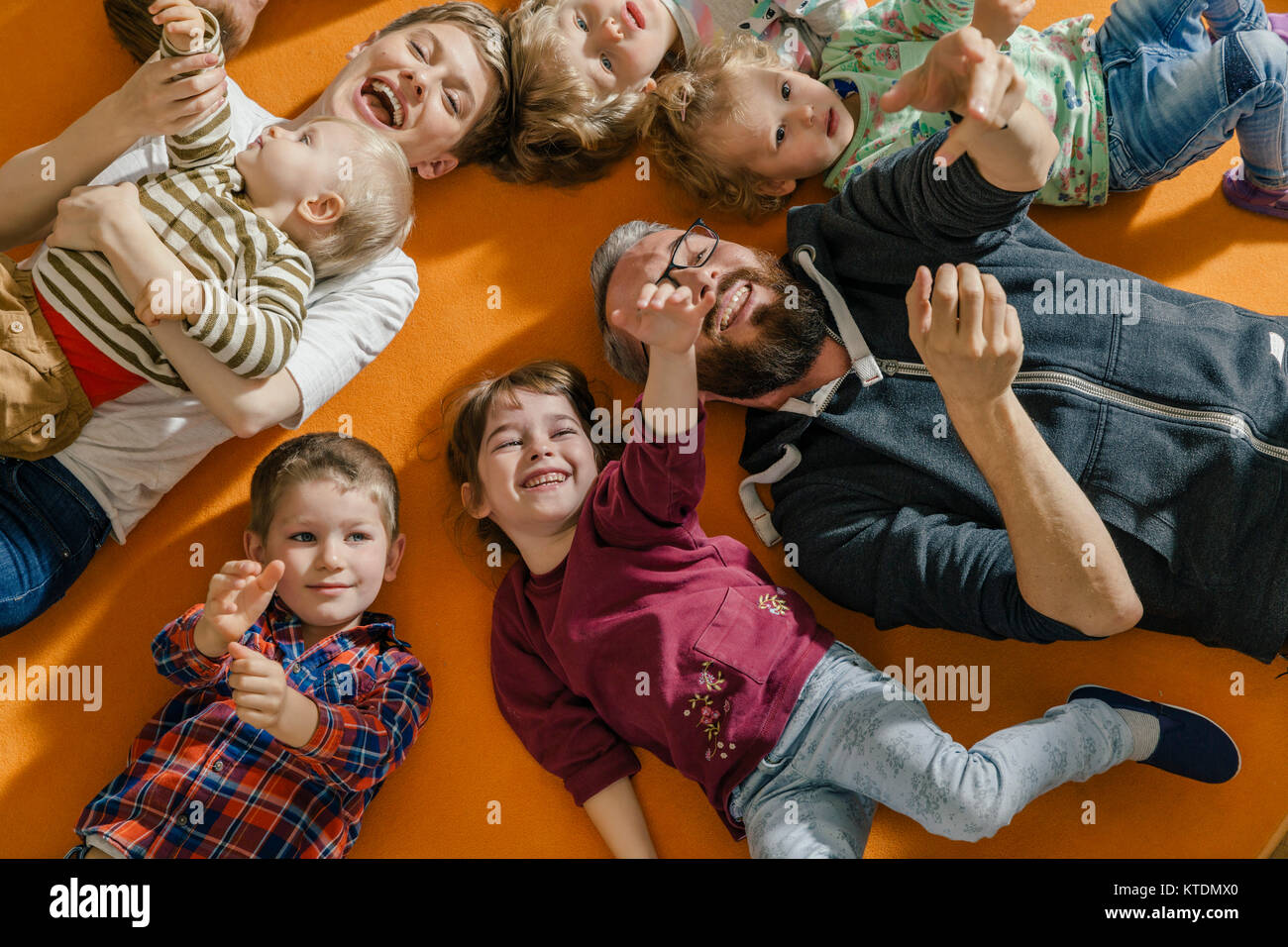 I bambini e gli insegnanti giacenti e cantare sul tappeto in kindergarten Foto Stock