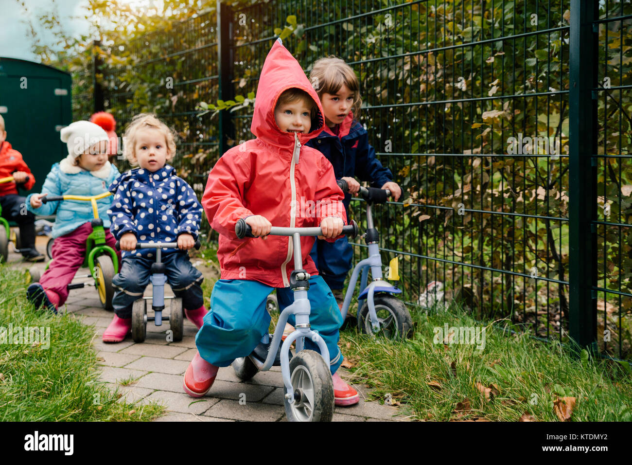 I bambini che usano gli scooter nel giardino di un asilo infantile Foto Stock