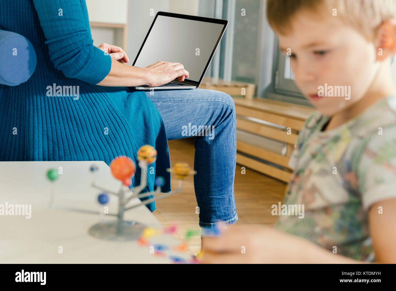 Ragazzo esplorazione del sistema solare con il modello di donna con il computer portatile in una scuola materna Foto Stock