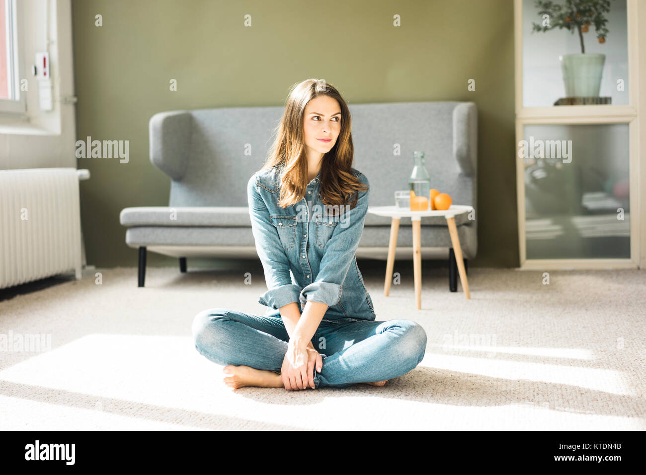 Giovane donna seduta sul pavimento nel soggiorno Foto Stock