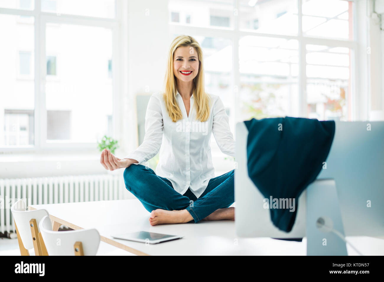 Imprenditrice sorridente seduto sulla scrivania in ufficio la pratica dello yoga Foto Stock