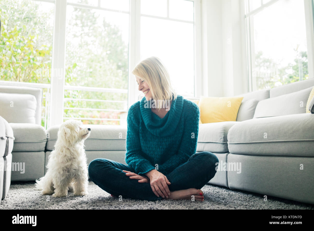 Donna sorridente guardando il suo cane nel soggiorno Foto Stock