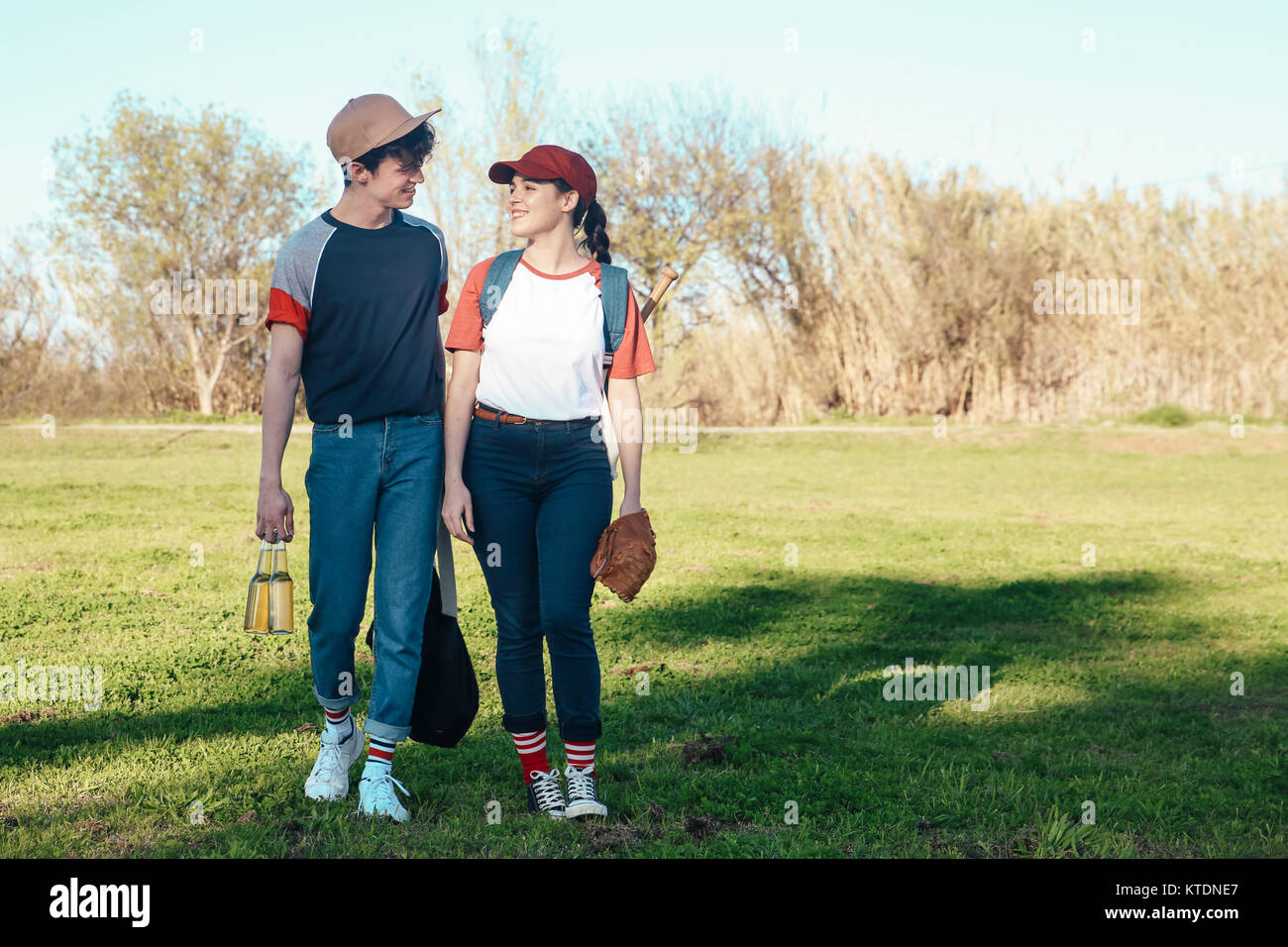 Sorridente coppia giovane con attrezzatura da baseball passeggiate nel parco Foto Stock