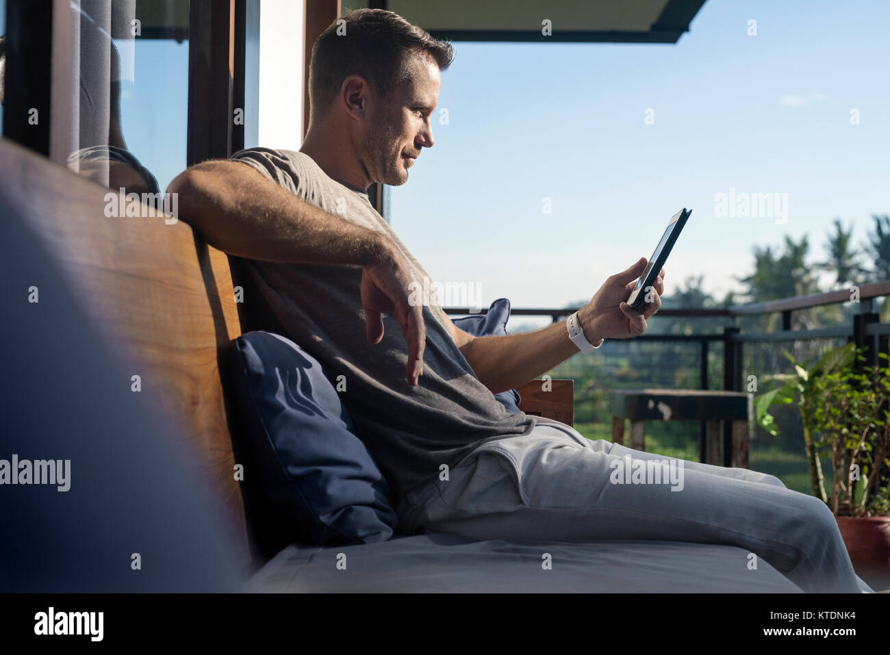 Uomo seduto sul balcone di casa moderna, guardando a smartphone Foto Stock