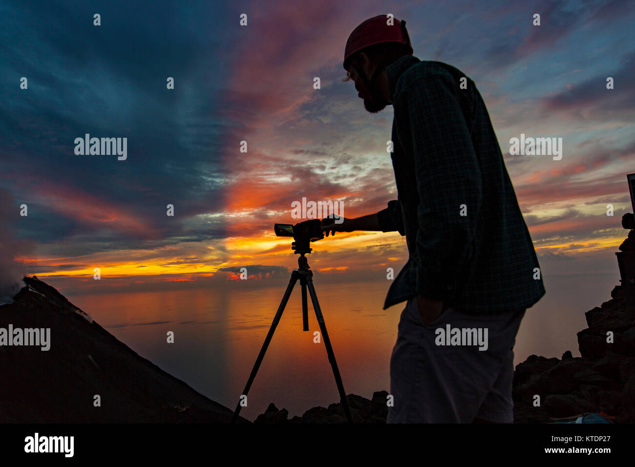 L'Italia, isole Eolie, Stromboli, giovane osservando eruzione vulcanica con tramonto colorato sfondo Foto Stock
