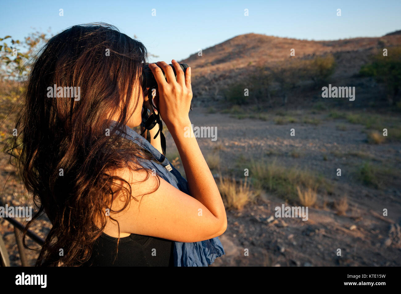 Giovane donna attraente guardare attraverso il binocolo - Huab sotto tela, Damaraland, Namibia, Africa Foto Stock