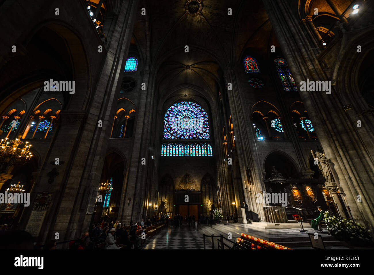 Servizi presso la cattedrale di Notre Dame a Parigi Francia evidenziando l'illuminazione drammatica all altare con molte finestre di vetro colorato e il rosone Foto Stock