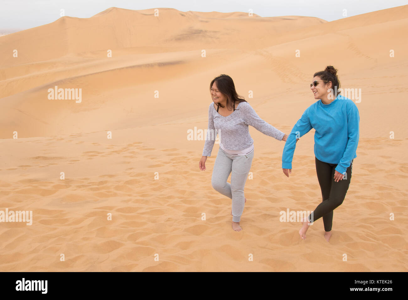 Due ragazze di diversa etnia divertendosi nel deserto sulle dune 7, Walvis Bay, Namibia Foto Stock