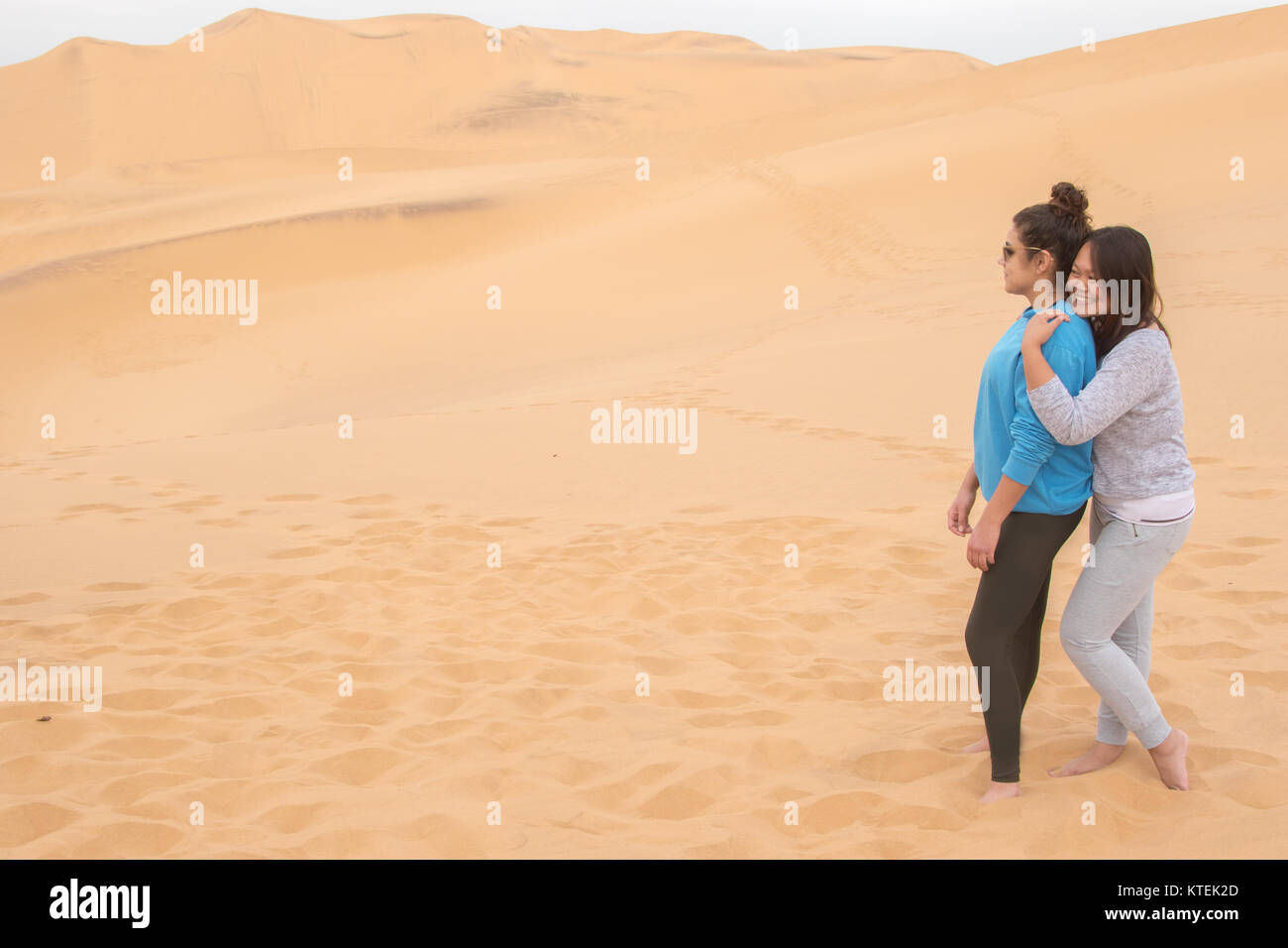 Due ragazze di diversa etnia divertendosi nel deserto sulle dune 7, Walvis Bay, Namibia Foto Stock