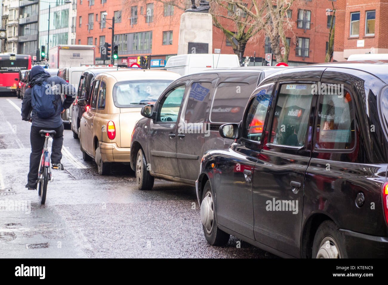 Ciclista uomo sulla bicicletta pedalando passato una fila di London Black Cab taxi su Holborn, Londra, Regno Unito Foto Stock