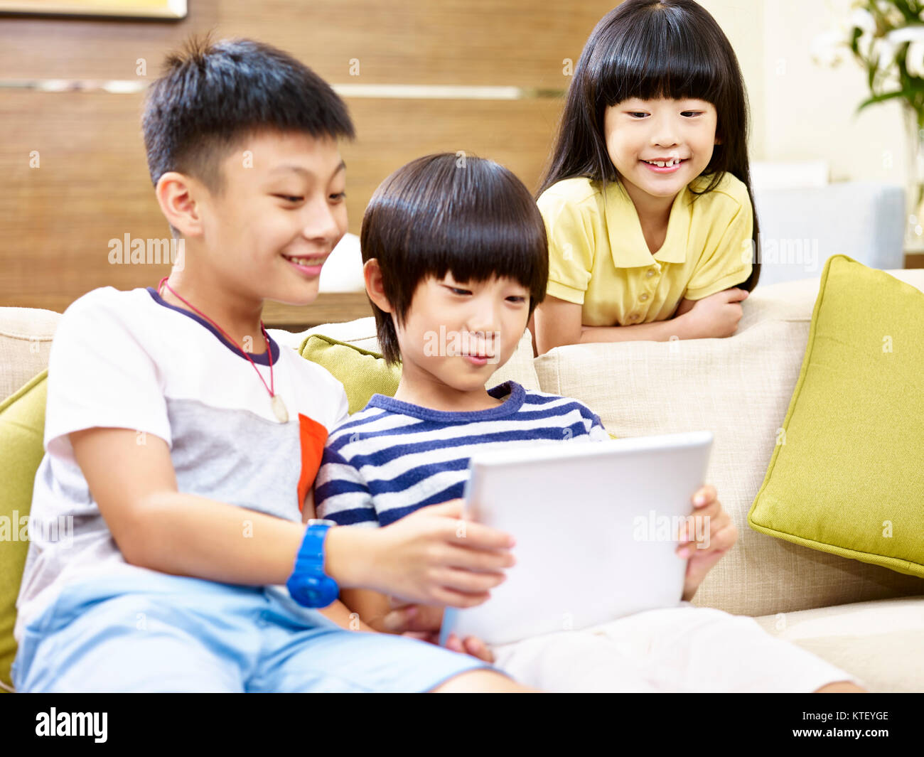 Tre bambini asiatici due little boy e una bambina seduti sul divano a casa la riproduzione del video gioco con tavoletta digitale, focus su la bambina in t Foto Stock