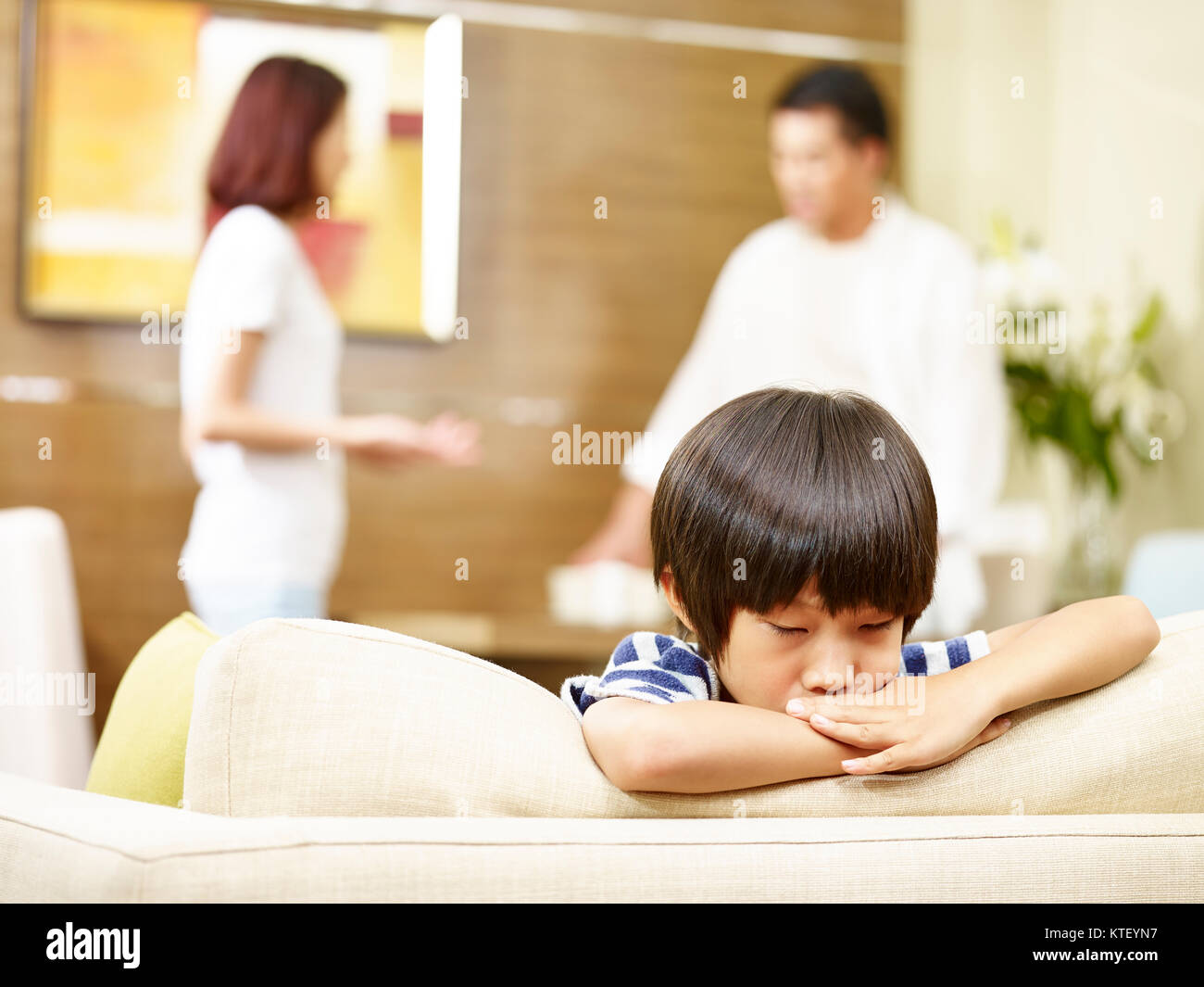 Bambino asiatico sembra triste e infelice mentre i genitori quarreling in background. Foto Stock