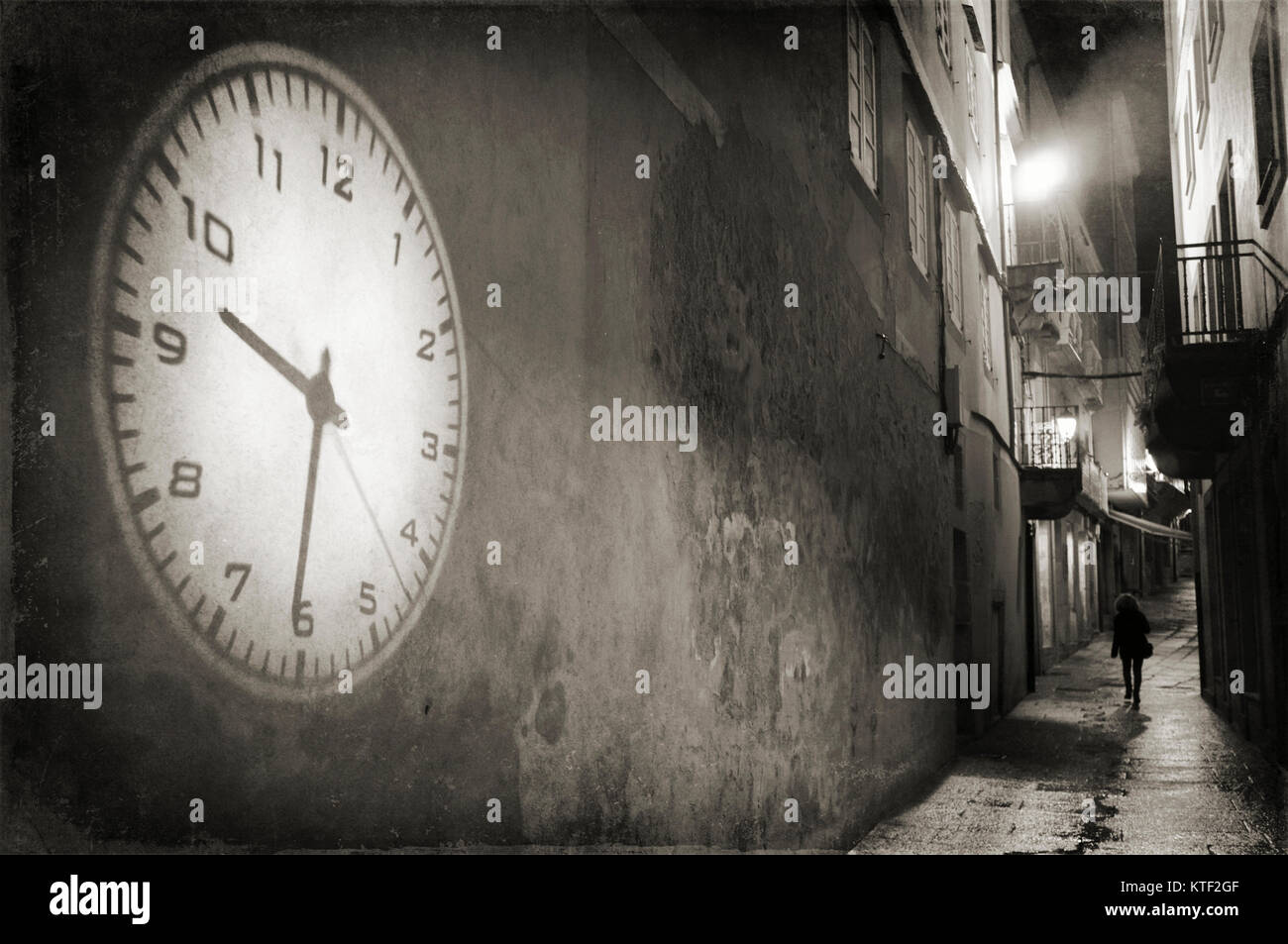 Lone Donna che cammina su un vicolo buio e la proiezione del grande orologio su una parete vuota. Città vecchia di Viveiro, provincia di Lugo, Galizia, Spagna, Europa Foto Stock