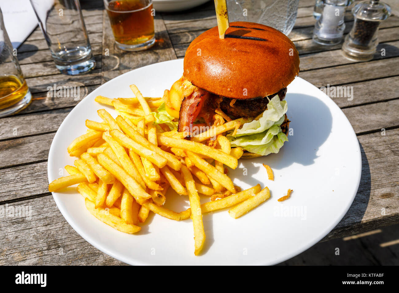 Obesità: tipico pub britannico cibo: un beefburger in un panino con il formaggio e la pancetta e una pila di golden patatine fritte, hamburger e patatine su una piastra bianca Foto Stock