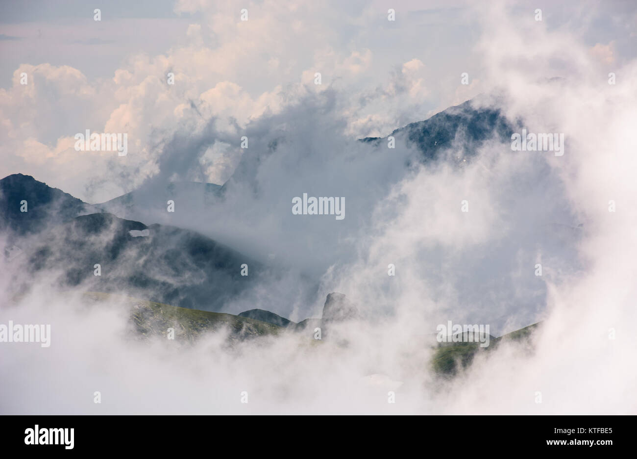 La formazione di nubi in montagna in alta altitudine. spettacolare fenomeno naturale in estate. Il tempo è stato molto bello sfondo di colline con neve ed erba Foto Stock