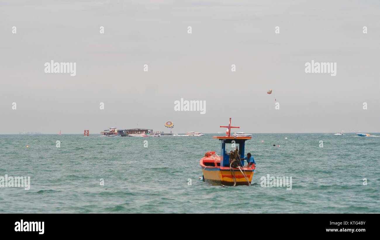 Barca piccola di colore arancione Golfo della Thailandia Shoreline a Beach Road Pattaya Thailandia parasailing sullo sfondo Foto Stock