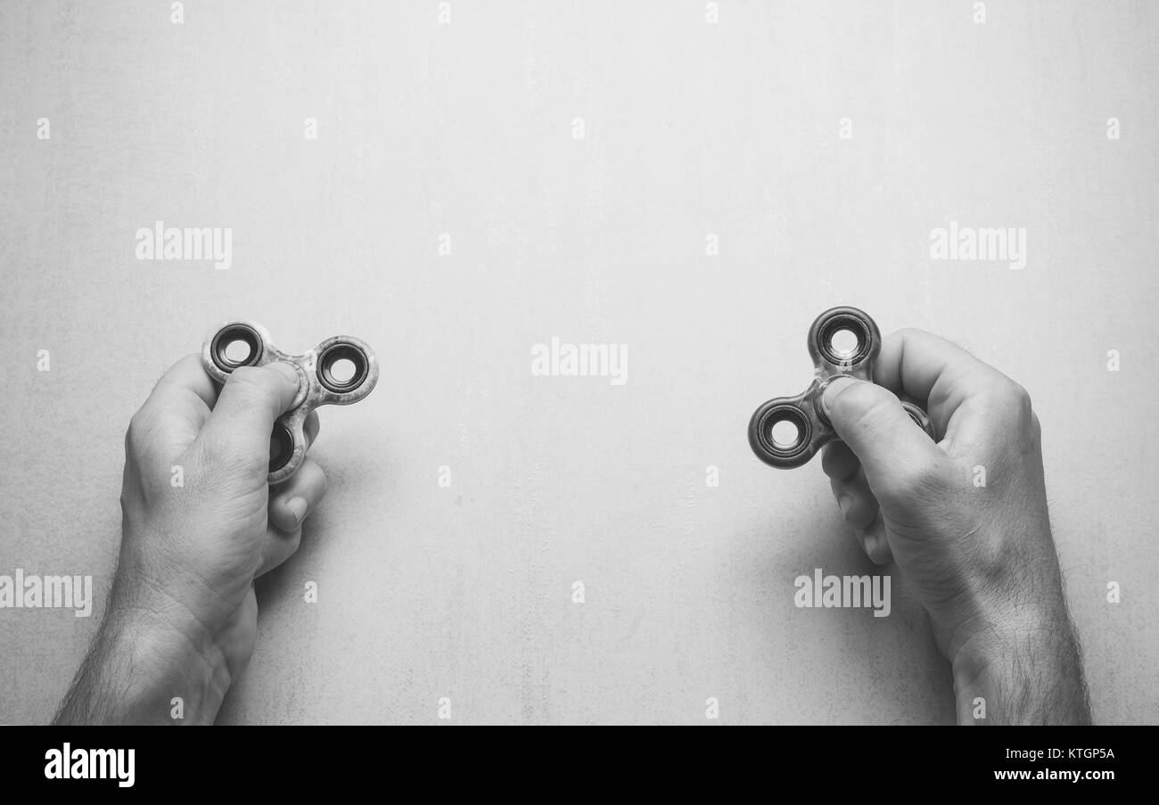 Gli uomini con le mani agitano: popolare giocattolo spinner su uno sfondo grigio con spazio per il testo vista superiore, foto in bianco e nero. mock up per testo, frasi letteri Foto Stock