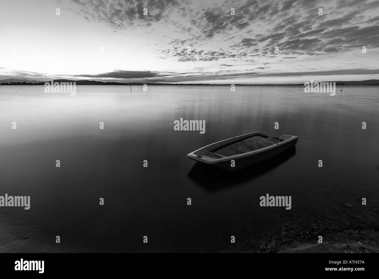 Una piccola barca da pesca nel mezzo di perfettamente ancora acqua al tramonto, con sgombri nuvole sky (lago Trasimeno, Umbria, Italia) Foto Stock