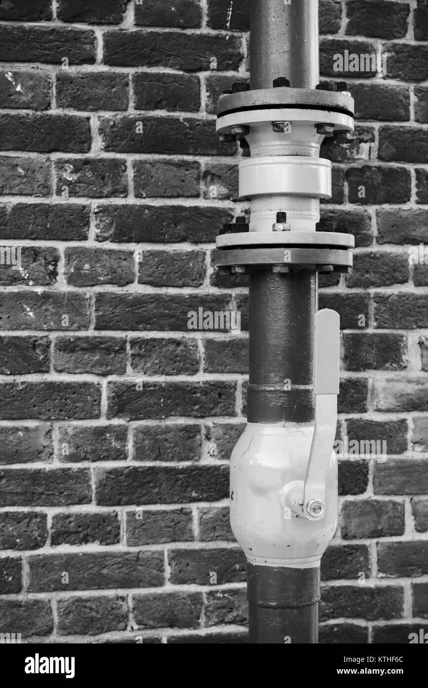 Tubo del gas con valvola aperta al di sopra di un muro di mattoni, foto in bianco e nero Foto Stock