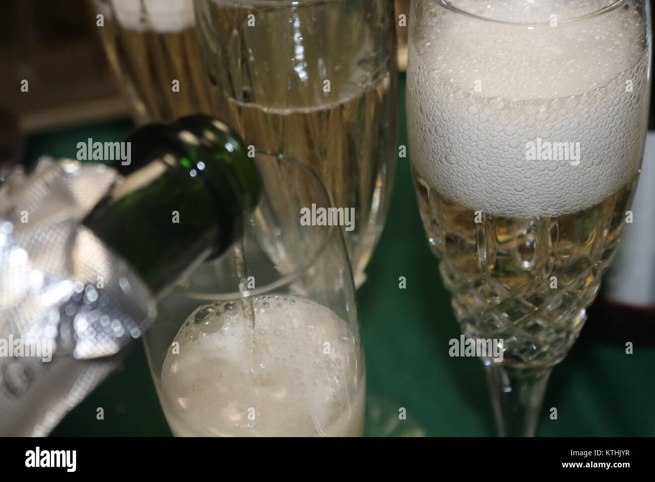 Bolle coming off versata una bottiglia di champagne in un vetro schiumoso con bottiglia circostante forme e più champagne venga versato Foto Stock