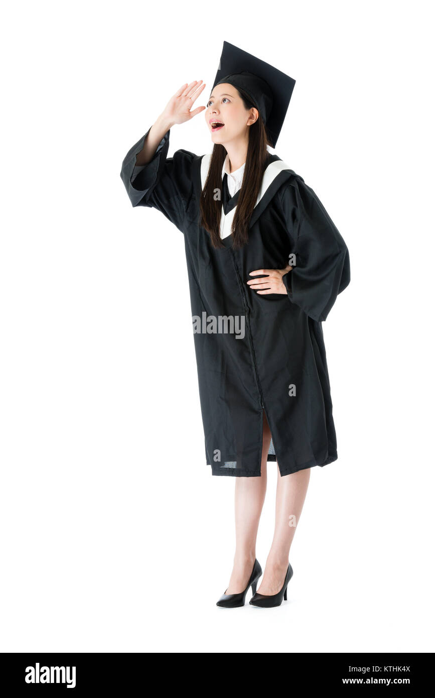 Attraente femmina giovane studente di college finito di studiare indossando indumenti di graduazione in piedi su sfondo bianco e guardando a distanza pensando fu Foto Stock