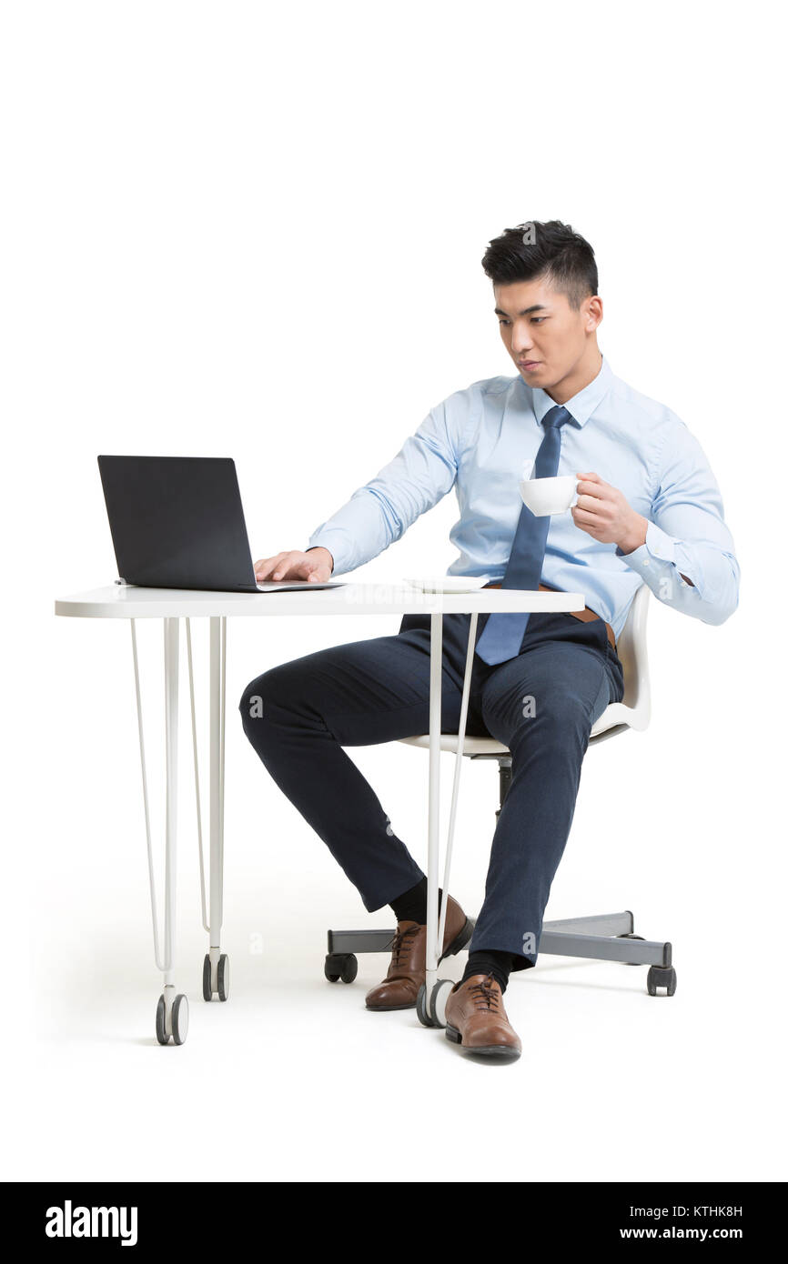 Giovane imprenditore lavora con il computer portatile in ufficio mentre beve caffè Foto Stock