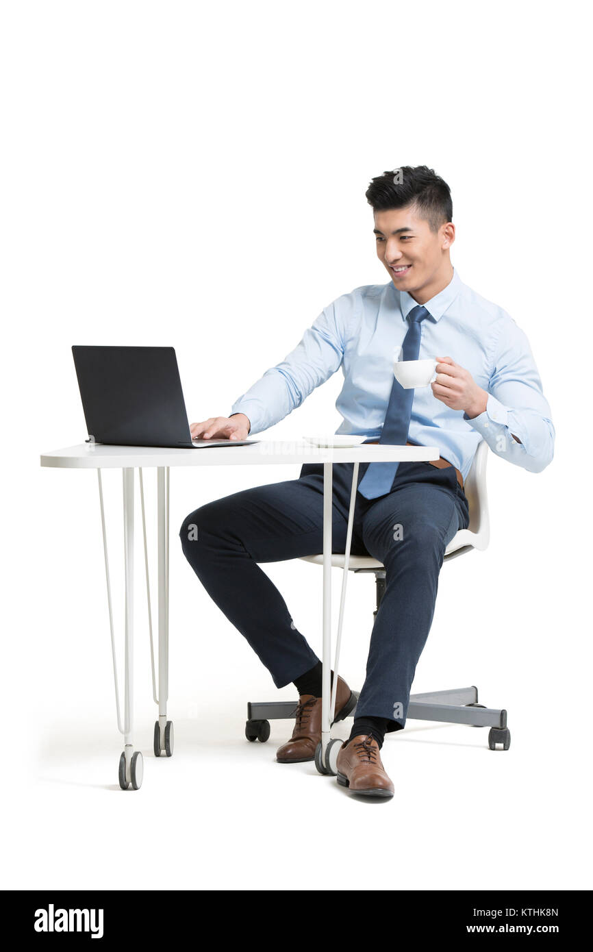 Giovane imprenditore lavora con il computer portatile in ufficio mentre beve caffè Foto Stock