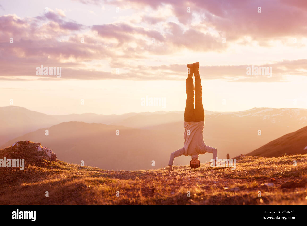 L uomo sta capovolto sulla vetta della montagna al tramonto sullo sfondo Foto Stock