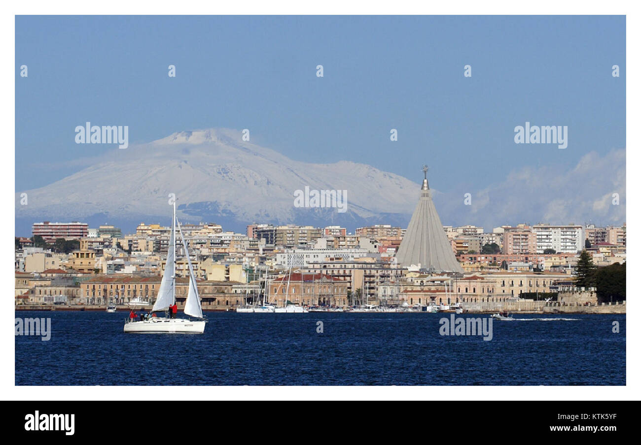 Questa immagine presenta una barca a vela vicino al santuario dell'Etna, visibile dal grande porto di Siracusa in Sicilia, Italia. Mette in evidenza la bellezza costiera e le caratteristiche naturali della regione. Foto Stock