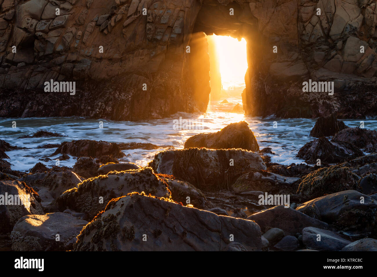 La luce del sole e navigare in streaming tramite toppa Arch a Pfeiffer Beach lungo la California's Big Sur Costa nei giorni precedenti e seguenti il winter s Foto Stock