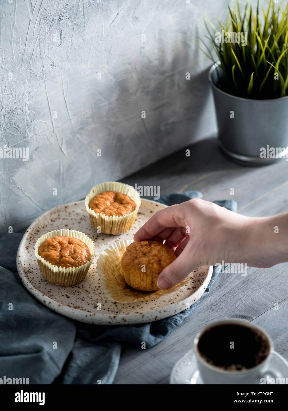 Muffin fatti in casa sulla piastra di artigianato grigio su un tavolo di legno. Tenere in mano la carota tortina. Copia dello spazio. Immagine dai toni in stile scandinavo. Foto Stock