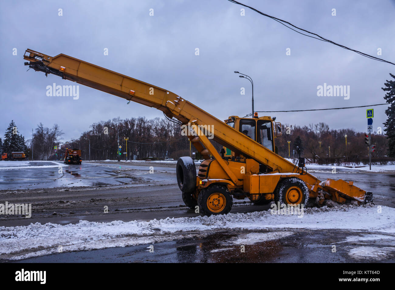 Macchina pale da neve sulla strada e il caricamento di neve in un carrello . Macchine arancione, neve pulitori , vicino al semaforo . Mosca , Russia . Foto Stock