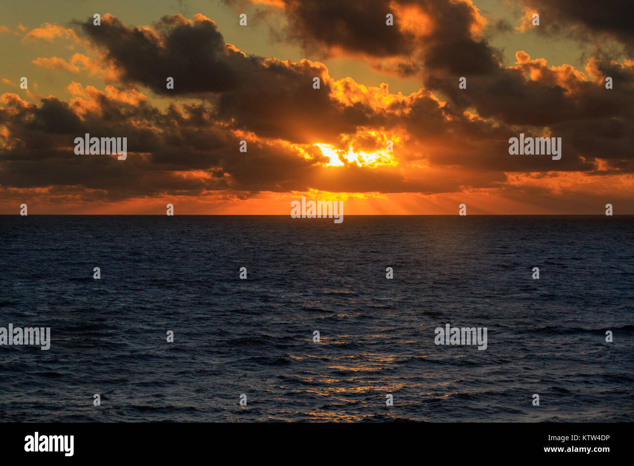 Mentre a vela attraverso il profondo blu dell'Oceano Atlantico sorge il sole attraverso le nuvole con una magnifica luce calda Foto Stock