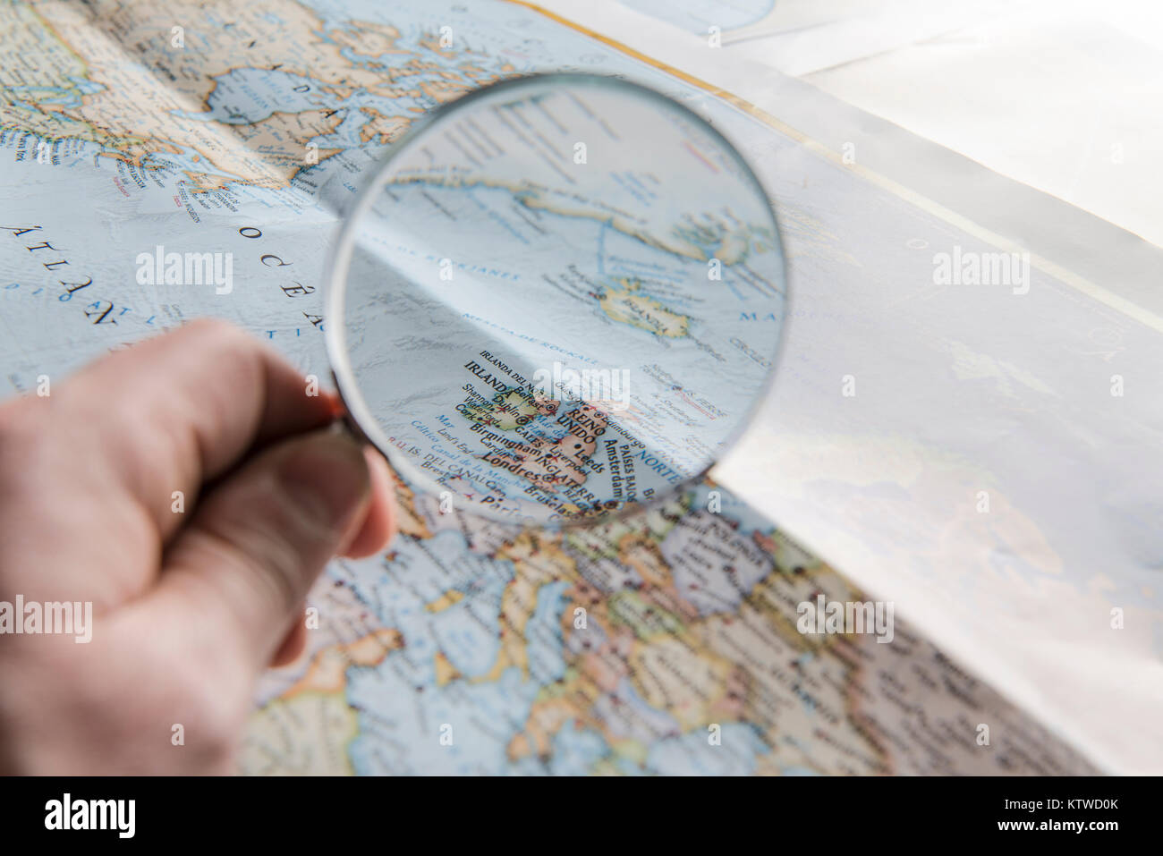 Fotografia a colori di una mano che tiene una lente di ingrandimento con una mappa in background. Foto Stock