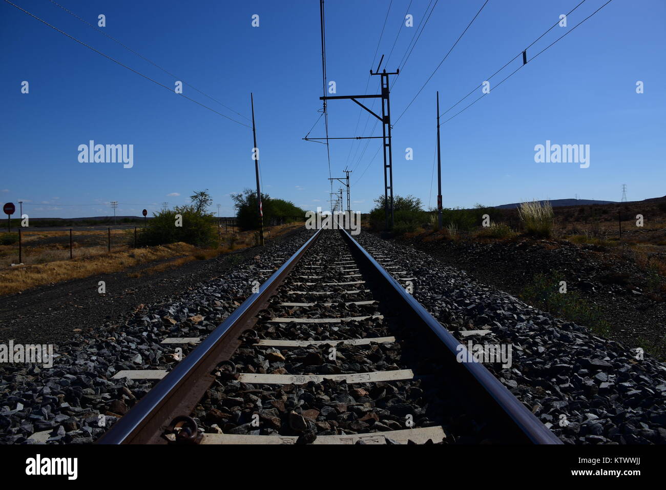 Binari del treno girato a basso angolo convergenti in un punto di fuga all'orizzonte con un cielo blu sopra Foto Stock