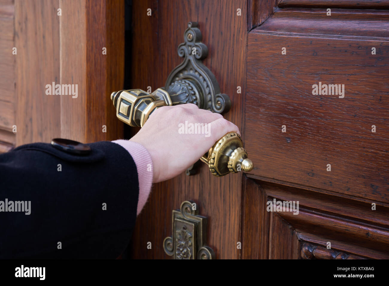 Una femmina la mano che regge una manovella da una vecchia porta di legno e apertura Foto Stock