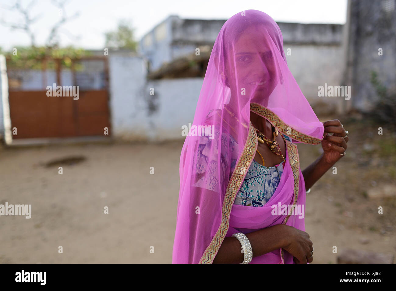 Ritratto di giovane donna indiana indossando sari e una rosa velo che copre il volto nel suo cortile, villaggio nei pressi di Pushkar, Rajasthan, India. Foto Stock