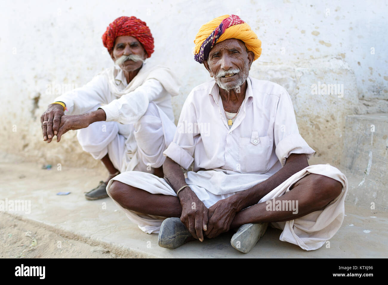 Due senior Indian uomini in bianco, indossa turbanti e big mustaches, seduto su un marciapiede in un villaggio nei pressi di Pushkar, Rajasthan, India. Foto Stock