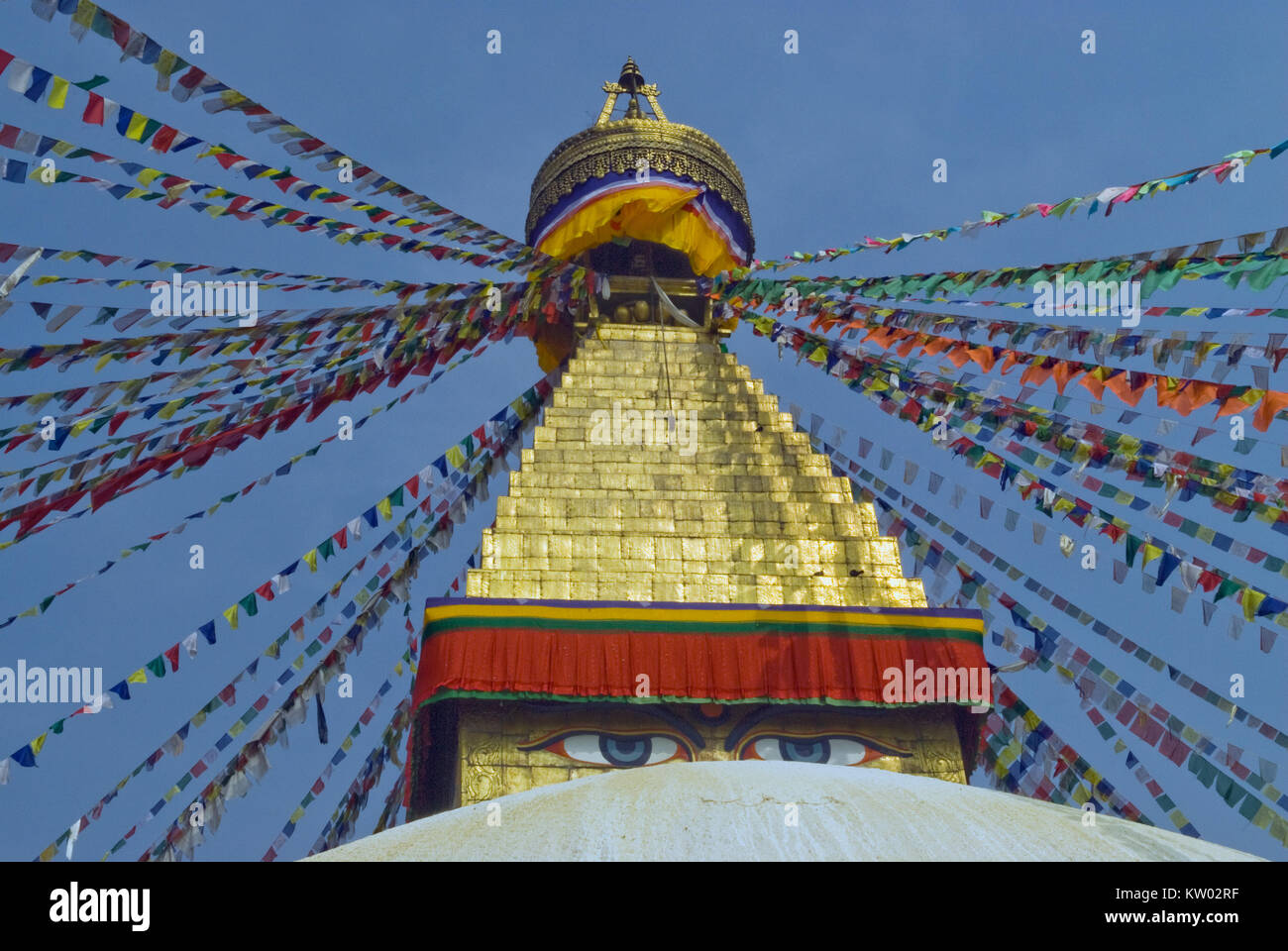 Parte superiore della stupa buddisti Bodnath: la cupola dorata e il Buddha gli occhi al di sotto di essa, la preghiera bandiere tibetano in diverse direzioni divergenti contro Foto Stock