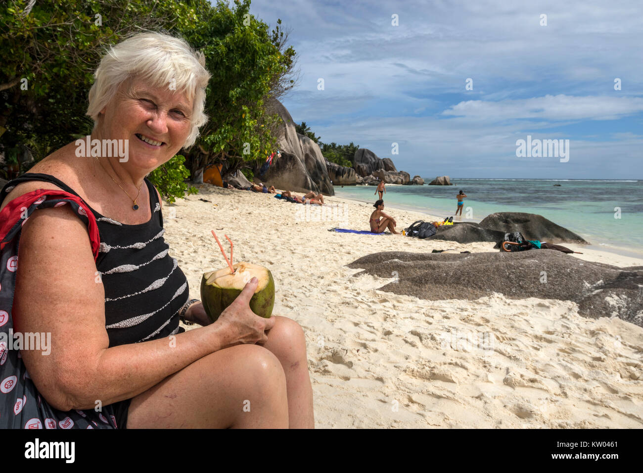 Donna di bere con una cannuccia dal succo di cocco, latte di cocco sulla spiaggia di Anse Source d'Argent, La Digue, Seicelle Foto Stock