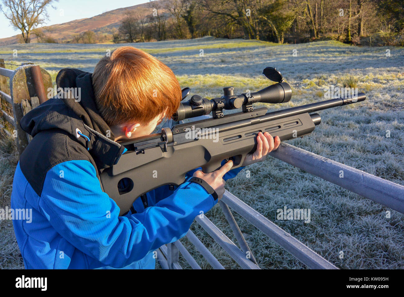 Ragazzo adolescente sparando un fucile ad aria compressa su terreno coltivato su un freddo gelido giorno. Foto Stock